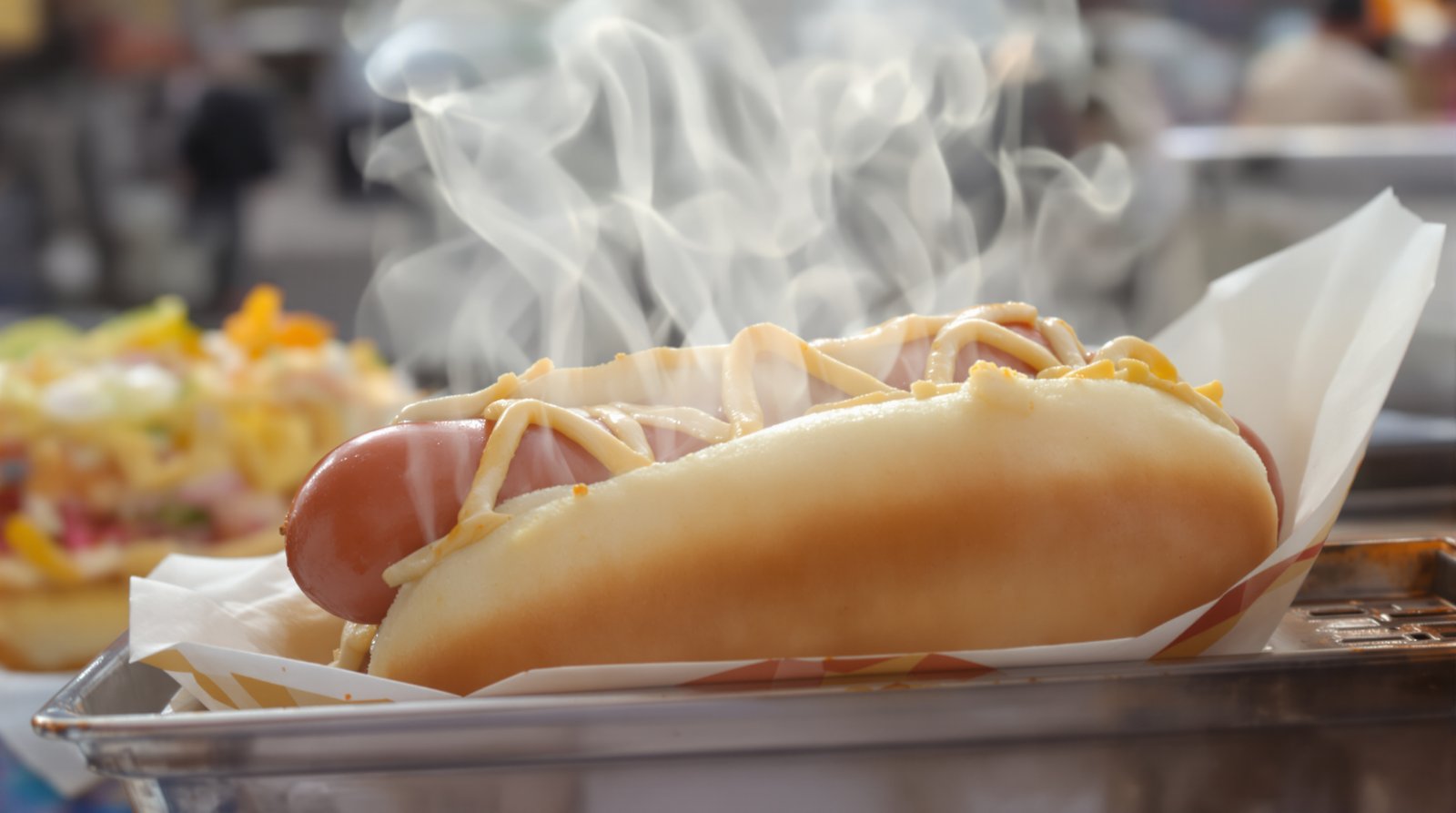A close-up, high-detail shot of a classic New York hot dog from a street vendor's cart, with steam rising