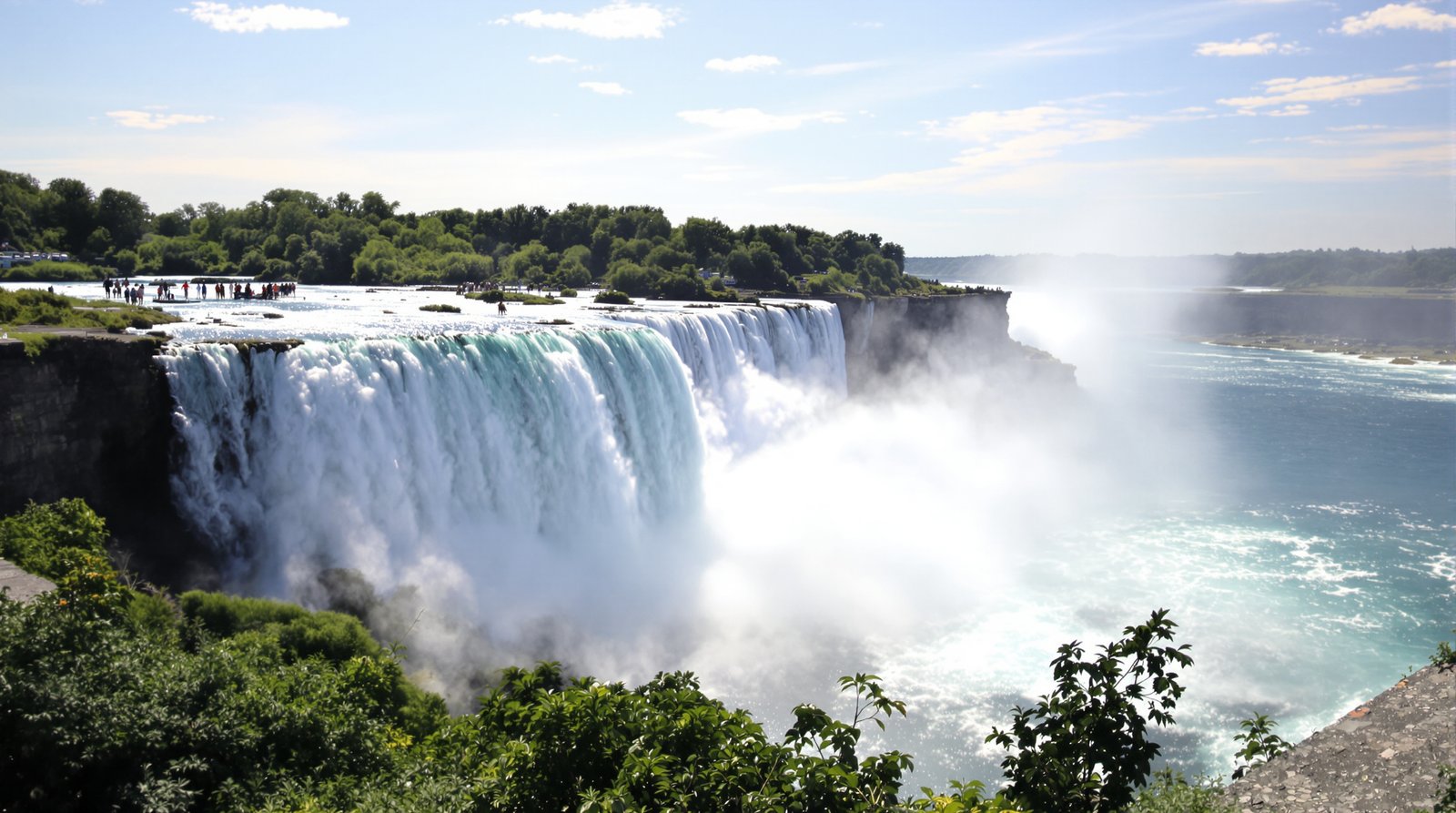 A powerful, wide-angle view of Niagara Falls, with mist rising from the cascading water under a clear sky