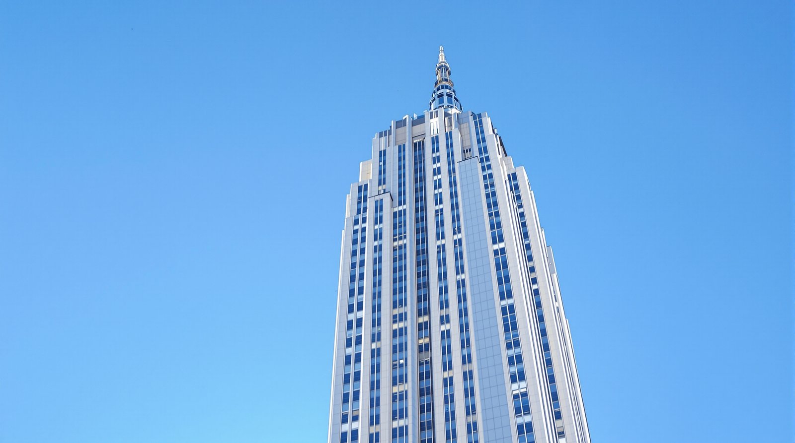 An ultra-realistic, professional travel photograph of the Empire State Building, shot from a low angle against a clear blue sky, emphasizing its Art Deco details and immense height