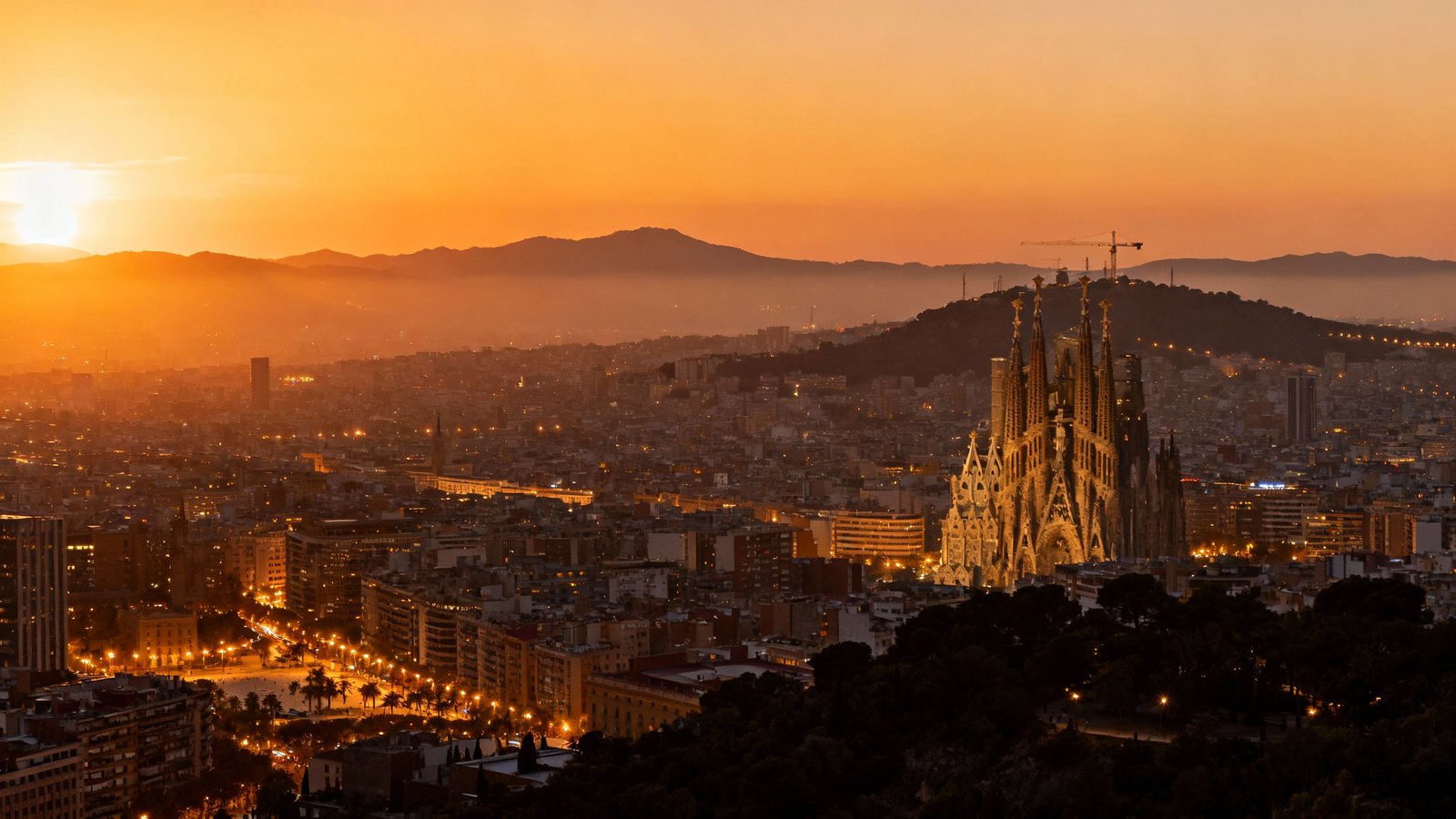 A stunning panoramic skyline view of Barcelona at sunset from a high vantage point like the Bunkers del Carmel or Tibidabo, with the city lights beginning to twinkle