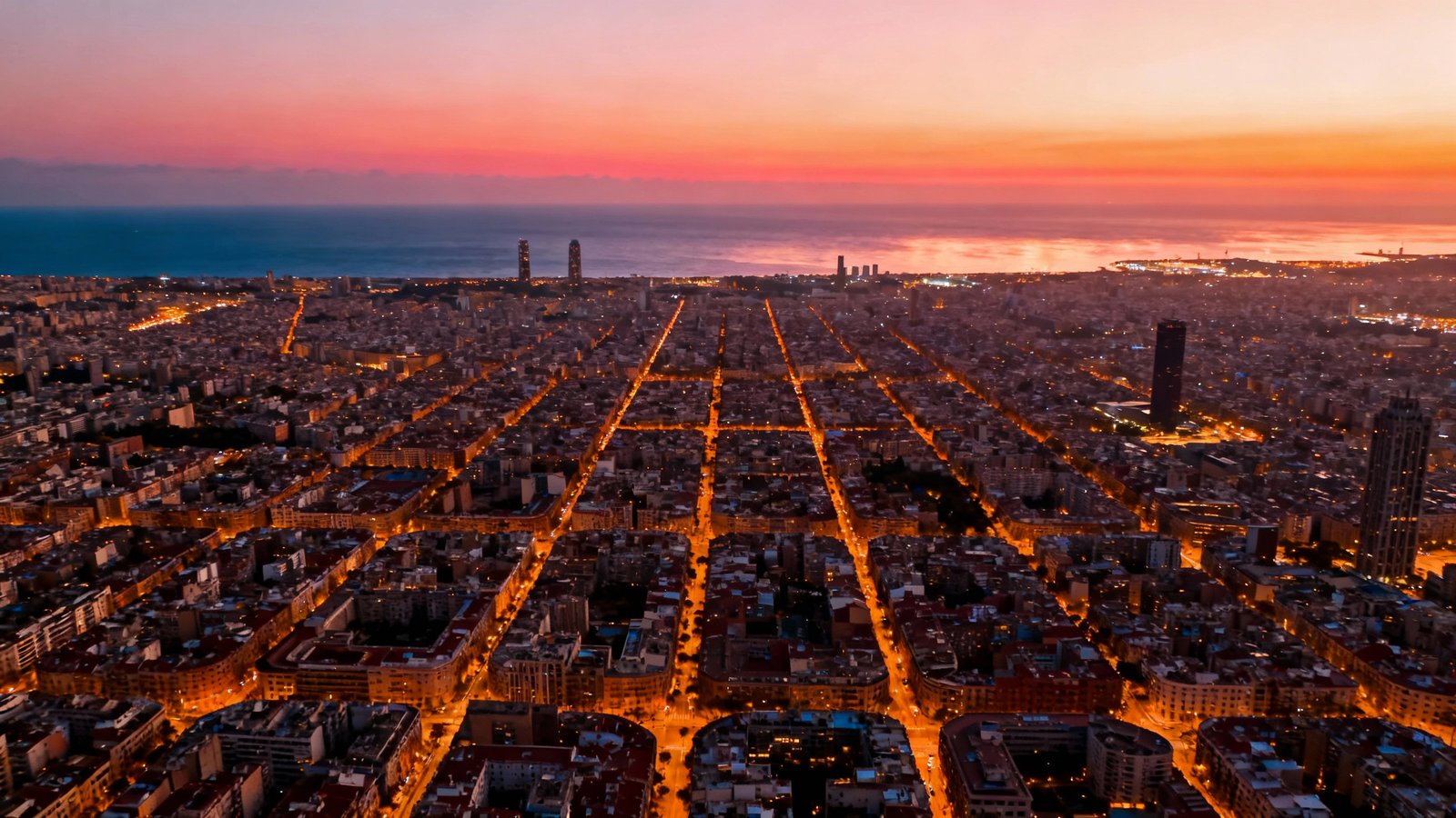 Cinematic wide-angle shot of the Barcelona skyline from the Bunkers del Carmel at sunset, showing the city grid and the sea beyond