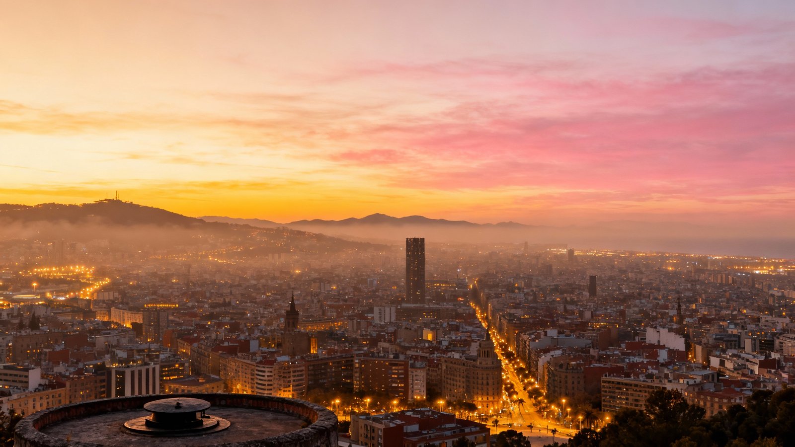A stunning panoramic skyline view of Barcelona at sunset from a high vantage point like the Bunkers del Carmel, with the city lights beginning to twinkle