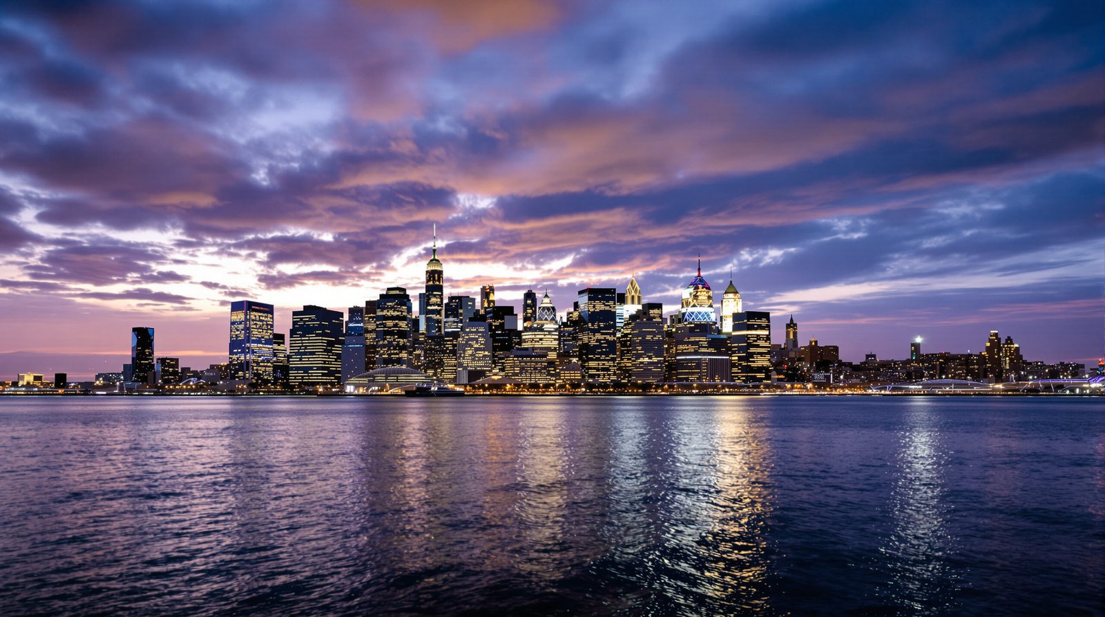 A stunning, cinematic wide-angle shot of the Manhattan skyline at dusk, with the lights of skyscrapers reflecting on the water