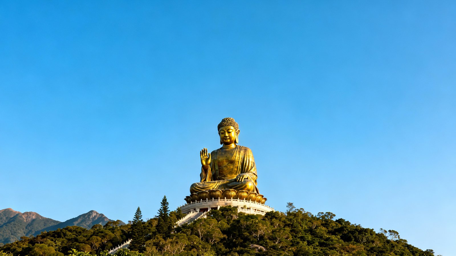 The majestic Tian Tan Buddha statue sitting atop a hill on Lantau Island, viewed from below with a clear blue sky