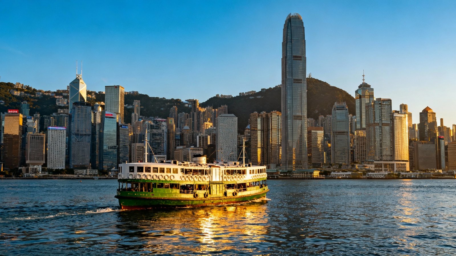 The iconic green and white Star Ferry crossing Victoria Harbour, with the dramatic Hong Kong Island skyline in the background, shot from the Tsim Sha Tsui side on a clear day