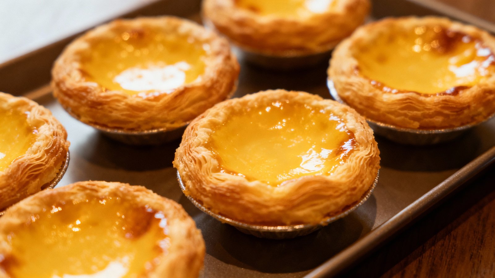 A close-up of golden, flaky Hong Kong-style egg tarts on a tray