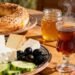 Ultra-realistic Turkish breakfast spread: simit, cheeses, olives, tomatoes, cucumbers, honey, and steaming Turkish tea, set on a bright, sunlit table with traditional Turkish crockery